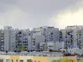 Rząd szarych bloków z wielkiej płyty, z balkonami i antenami, pod pochmurnym niebem.