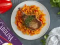 Chuleta de cerdo jugosa sobre arroz rojo con pimientos.