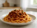 Talerz spaghetti z bogatym sosem mięsnym ragù, udekorowany zielonymi listkami.