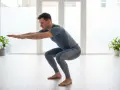 Un homme en tenue de sport exécute un squat dans une pièce lumineuse.