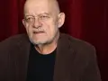 Siwy, łysy mężczyzna z brodą, ubrany w brązową marynarkę i czarną koszulkę. To znany ferency aktor.