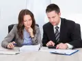 Dos profesionales concentrados revisan documentos y utilizan una calculadora para contabilizar facturas de años anteriores.