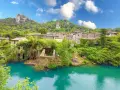 Un borgo incantevole in Umbria, con case in pietra ricoperte di vegetazione che si affacciano su un fiume turchese. Un luogo perfetto per i cammini.