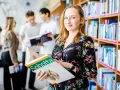 Studentka na Uniwersytecie Wrocławskim, kierunek prawo, przegląda atlas anatomii. W tle inni studenci i regały z książkami.