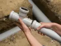 Ręce łączą elementy instalacji wodnej w domu. Montaż rur kanalizacyjnych w wykopie.