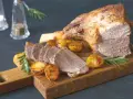 Un gigot de 7 heures, tendre et juteux, servi avec des pommes de terre rôties et du romarin sur une planche en bois.