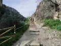 Senderos de montaña con escalones de piedra y madera. Personas caminan por las rutas Patones de Arriba, rodeadas de vegetación y acantilados.