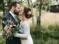 Para młoda całująca się na tle natury. Ona w koronkowej sukni, z kwiatami we włosach. On w garniturze. Idealny przykład ślubu "stodołowego" w ubiorze.