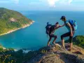 Due escursionisti si aiutano a salire su una scogliera con vista su una baia tropicale. Questo è il trekking cos'è: avventura e collaborazione.
