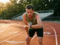 Un coureur essoufflé sur une piste d'athlétisme, vérifiant sa montre après une séance VMA intense. Le soleil couchant illumine la scène.