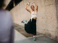Joven sonriente con falda escocesa y top blanco, luciendo unos modernos looks con zapatillas deportivas.