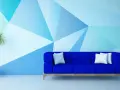 Nowoczesna ściana z geometrycznymi wzorami z farby w odcieniach niebieskiego, z niebieską kanapą i rośliną.