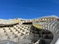 The Metropol Parasol, known as Las Setas de Sevilla, features a modern wooden structure with winding walkways and yellow steps under a clear blue sky.