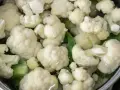 Kalafior gotuje się w garnku z wodą. Białe różyczki i zielone liście są zanurzone w płynie.