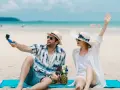 Para na plaży nagrywa filmik kamerką GoPro, a jego partnerka macha do obiektywu. Idealne wakacje pod gruszą!