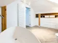 Élégante salle de bain sous pente avec baignoire îlot, lavabo, toilettes et rangements en bois.