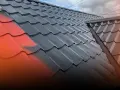 Malowanie dachu z blachy: połowa pokryta czarną farbą, druga połowa wciąż czerwona.