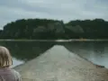 Dziewczyna z blond włosami patrzy na spokojną taflę jeziora, czując uczucie pustki.