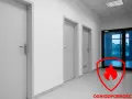 Korytarz z kilkoma drzwiami, w tym jedne przeszklone. Czerwona tarcza z płomieniem symbolizuje ognioodporność, ważne przy wyborze drzwi do kotłowni.