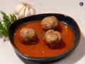 Tres albóndigas caseras en una rica salsa de tomate, adornadas con perejil fresco. Un plato reconfortante que evoca la cocina tradicional.