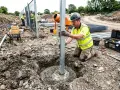 Budowlaniec sprawdza pion słupa ogrodzeniowego, który jest osadzany w betonie. To kluczowy etap budowy, gdzie fundament punktowy rozstaw jest precyzyjnie wykonany.