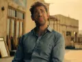 John Krasinski w niebieskiej koszuli, zamyślony. Widzimy fragmenty jego filmów, seriali i programów.