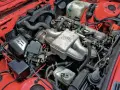 Silniki BMW E30 w czerwonej komorze silnika. Widoczny kolektor ssący z logo BMW, chłodnica, akumulator i inne elementy układu napędowego.