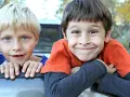 Dwóch chłopców, jeden z blond włosami i niebieskimi oczami, drugi z brązowymi włosami i szerokim uśmiechem. Ich żywe spojrzenia mogą przypominać objawy ADHD u 2 latka, pełne energii i ciekawości świata.