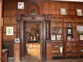 Wnętrze biblioteki w **zamku w Lubniewicach**. Drewniane boazerie, regały z książkami i portretami, a w przejściu widok na schody i sprzęt nagraniowy.