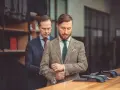Elegancki garnitur dla świadka, dopasowywany przez krawca. Mężczyzna z wąsikiem przymierza tweedową marynarkę w kratę.