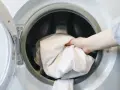 Ręka wkłada białe prześcieradło do pralki. Zastanawiasz się, w ilu stopniach prać ubrania? Sprawdź metkę!