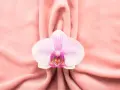 Delikatna orchidea na różowym tle, symbolizująca piękno i kobiecość, nawiązuje do tematu wycinania warg sromowych.
