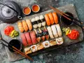 Piękny zestaw sushi: nigiri z łososiem, krewetkami, tuńczykiem i węgorzem, a także rolki. Obok czajniczek i filiżanki z herbatą. Idealne na co do sushi.