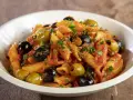 Penne con sugo rosso, olive nere e verdi, capperi e prezzemolo. Un piatto di pasta alla puttanesca invitante e saporito.