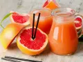 Orzeźwiający drink z grejpfrutem, podany w dzbanku i szklance, otoczony świeżymi owocami. Idealny na upalne dni.