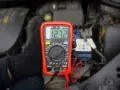Multimetr pokazuje 12.72V, co oznacza prawidłowe napięcie akumulatora. Sprawdzanie stanu baterii przed podróżą.