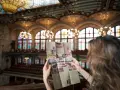 Kobieta studiuje broszurę z widokiem na wspaniałe wnętrze Pałacu Muzyki Katalońskiej, z witrażowym sufitem i rzędami siedzeń.