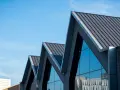 Nowoczesny budynek z ostrymi, geometrycznymi dachami. Zastanawiasz się, jak obliczyć kąt nachylenia dachu?