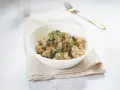 Miseczka kremowego risotto z grzybami, posypana ziołami i pieprzem, obok złoty widelec.