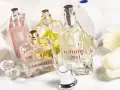Mehrere Parfümflaschen, darunter Trussardi und Tommy Girl, auf weißem Handtuch mit weißen Tulpen.