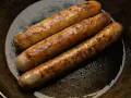 Drei goldbraune Bratwürste brutzeln in einer Pfanne. Perfekt für leckere Bratwurst Rezepte!
