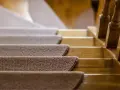Ciepłe, brązowe schody z wykładziny prowadzą w górę, obok drewnianej balustrady.