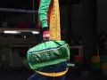 Zielony worek z napisem "UNITED COLORS OF BENETTON" niesiony przez modela w kolorowym swetrze.