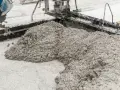 Beton wylewany z betoniarki na podłoże z drobnego kruszywa. Widać formę do wylewania betonu i masę, która tworzy kopiec.
