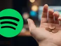Spotify-Logo neben einer Hand mit wenigen Cent. Ein Cent pro Stream ist wenig.