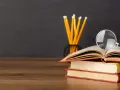 Stos książek, ołówki i lupa na drewnianym blacie. Idealne narzędzia do nauki, a może zapowiedź zniżek dla nauczycieli?