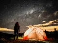 Nuit étoilée sur un bivouac GR34. Une personne admire la Voie lactée près d'une tente illuminée.