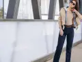 Kobieta w ciemnych jeansach straight, które podkreślają jej sylwetkę. Stylizacja uzupełniona beżową kurtką i okularami przeciwsłonecznymi.
