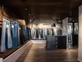 Jeans in vari lavaggi e tagli, inclusi modelli slim fit, esposti in un negozio moderno con pavimenti in legno scuro e illuminazione a faretti.