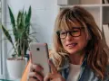 Kobieta w okularach przegląda telefon, być może szuka bratniej duszy na **Bumble w Polsce**.